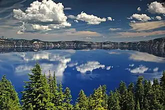 The water of Crater Lake can be seen above a forested area in the foreground.