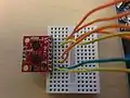 Take the IMU and flip it laterally, so the pins are now facing down. The front of the IMU will appear to be upside-down. Plug the IMU into the breadboard, with the first pin on top lining up with the first wire.